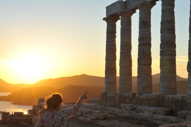 woman pointing at Grecian remains at sunset